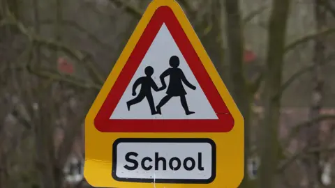 A yellow triangle 'children crossing' sign with 'School' below the sign in black text.