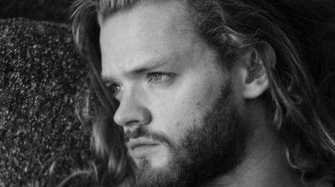 A black and white image of Fredrik Ferrier, who has long hair and a beard, looking into the distance