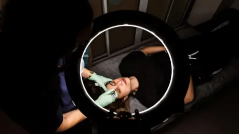 A woman lying on a bed having a beauty treatment. 