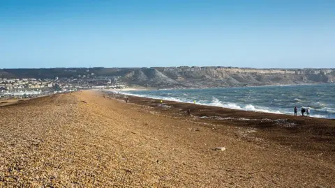 A shingle beach with white waves breaking on the shores with an island in the background