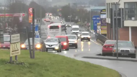 A number of cars, vans and busses are seen near a roundabout in Letterkenny.