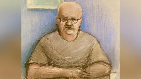 Elizabeth Cook/PA Media Court artist's image of Steve Wright wearing glasses and a T-shirt with his arms folded at a table during his appearance at Ipswich Magistrates' Court in June 2024