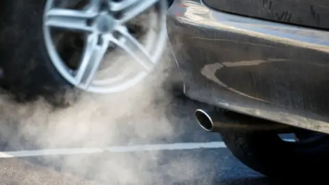 A picture of a car exhaust pipe, with a cloud of petrol or diesel coming out the back.