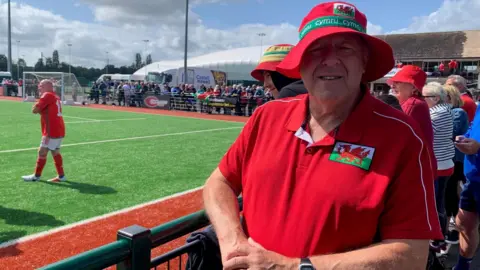 Fan Gary Bartlett poses in his red Wales bucket hat and Wales shirt next to the pitch