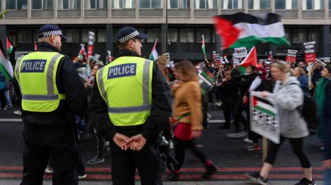 Two officers stand to the side as pro-Palestinian demonstrators walk past