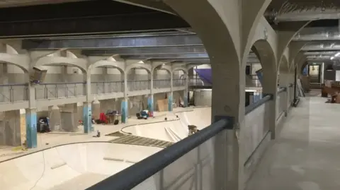 Source Park A large indoor skatepark under construction inside the former White Rock Baths in Hastings. The space features high arched concrete supports, walkways around the edge and skatepark ramps being built on the floor below.