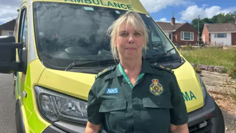 A woman in a green ambulance shirt standing in front of an ambulance