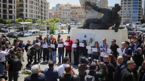 Reuters Journalists stand in a circle holding signs in front of a monument in Martyrs' Square, Beirut, in remembrance of Amal Khalil (23/04/26)