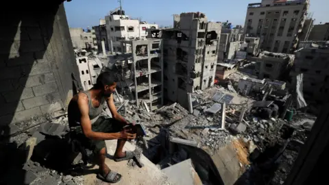 A Palestinian looks on at the site of an Israeli strike that destroyed residential buildings at al-Shati refugee camp, in northern Gaza (4 July 2025)