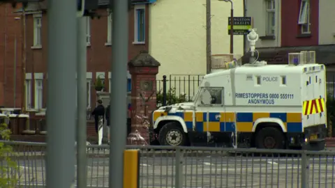 An armoured police vehicle parked on the pavement. There is paint splattered over the vehicle and on a nearby wall.