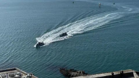 Royal Marines on board two high-speed boats come across the water in Plymouth Sound on a sunny day. Three buoys are behind them.