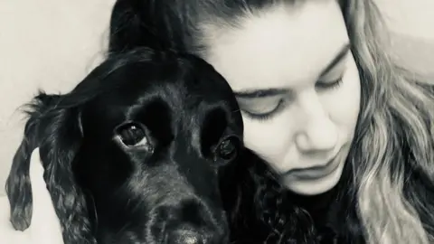 supplied A young woman with dark hair cuddles up to a black dig with large flappy ears