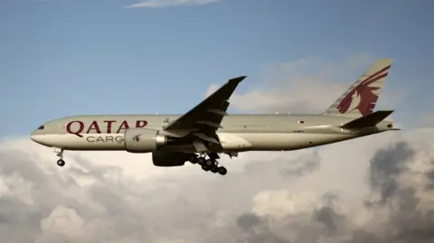  A Qatar Airways cargo Boeing 777 plane in a blue sky with white clouds