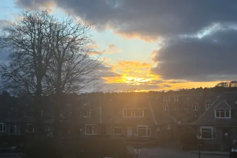 The glow of sunshine in the sky, behind clouds, over houses in Aberdeen.