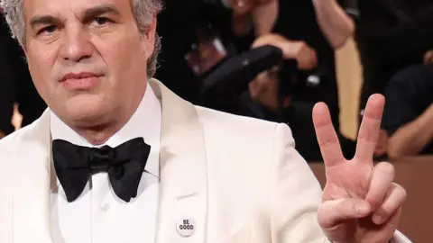 Getty Images Actor Mark Ruffalo wears a small badge which reads "Be good" on the lapel of his white tuxedo at the Golden Globe awards on 11 January. He holds up two fingers of his left hand to make the widely-recognised peace sign. 