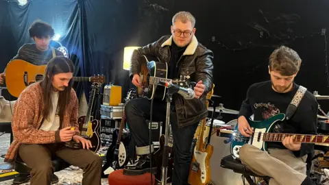 BBC Ryan Durrans, Scott Concepcion, Alex Moore and Matty Murphy from Wigan indie rock band The Lathums stand shoulder to shoulder in a recording studio and smile for a photograph 