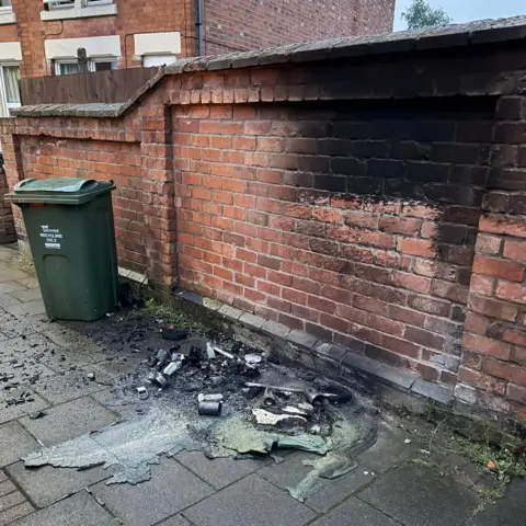 LFRS A green wheelie bin outside a property, which has smoke damage from another that was burnt next to it, in Loughborough, in Leicestershire, on Monday 4 May 2026.