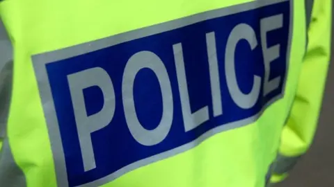 BBC The back of a police officer wearing a yellow and blue hi-vis jacket