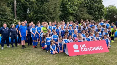 Dozens of young football players in blue and white kits gathered in a field for a photograph