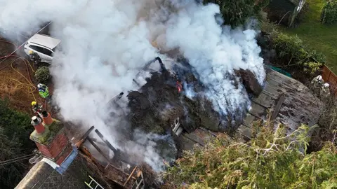 Aerial view of the fire-damaged property. Smoke is pouring from the rafters. 