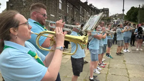 People all wearing blue polo shirts and a Scout neckerchief playing brass instruments