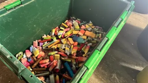 A green crate of disposable vapes of all colours. 