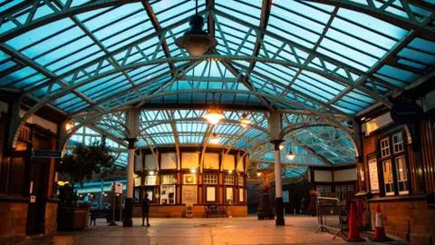 John McGuiness A railway station with a glass roof and vintage wooden ticket booths.
