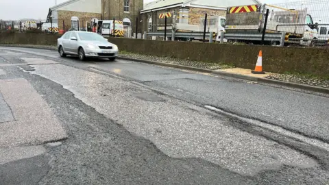 A car drives past a series of large potholes