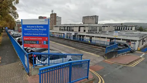 External view of the entrance and sign which reads 'Burnley General Teaching Hospital' showing vehicle parked outside the main building