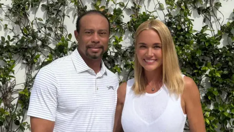 TIGER WOODS Tiger Woods and Vanessa Trump stand together in front of a wall covered by leaf trellises