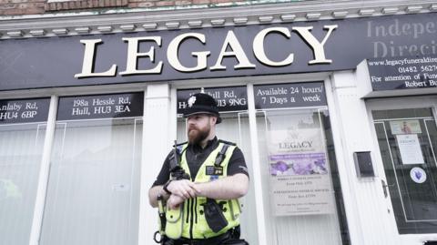 A police officer standing outside a branch of the Legacy Independent Funeral Directors