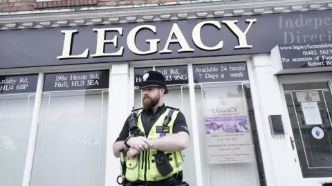 PA Media A police officer standing outside a branch of the Legacy Independent Funeral Directors