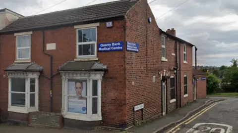 A red-brick building on a street corner with a blue sign saying 'Quarry Bank Medical Centre'.
