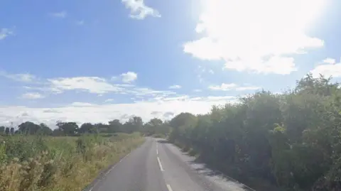 Google A country road, with tree and grass lining each side.