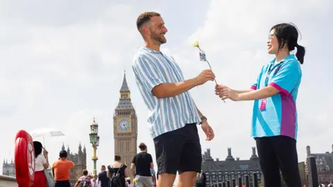 David Parry/PA Media Assignments for Hull Trains A Hull volunteer in a blue shirt handing a white rose to a man on Westminster Bridge with Big Ben in the background
