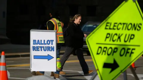 Getty Images Woman walks past a sign saying 'Ballot return'