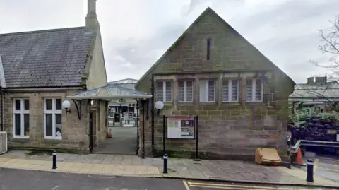 Google The entrance of platform 2 at Durham train station. Two beige stone building house the station cafe, waiting room and toilets. The glass entry barriers are in the distance. 