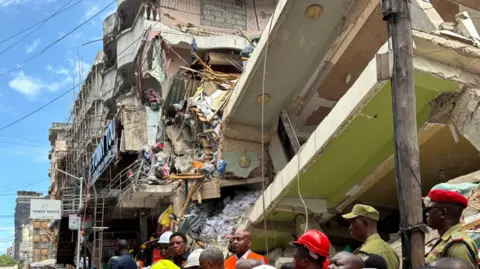 Rescuers stand near a collapsed building in the Kariakoo area of Dar es Salaam, Tanzania