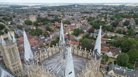 An aerial view of Lincoln Cathedral's central tower and pinnacles, towering above the city as maintenance workers carry out inspections high above the rooftops.
