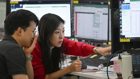 A woman in a red cardigan points to a screen during a discussion with a colleague in a trading room in Seoul 