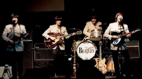 Three guitarists and a drummer playing on stage. The writing on the drumkit says "The Bootleg Beatles".