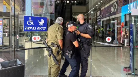 Israeli security forces stand at the entrance to a shopping mall in Karmiel, northern Israel, after a deadly stabbing attack (3 July 2024)