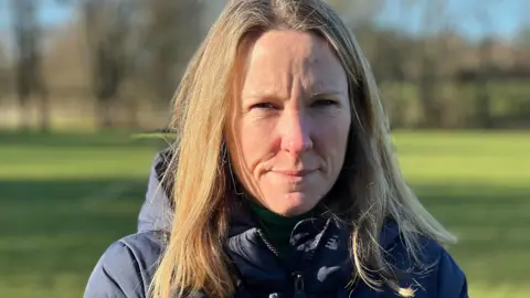 Michelle Ellis standing on the football playing fields, wearing a thick blue anorak 