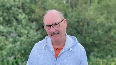 A man in a grey hoodie with glasses