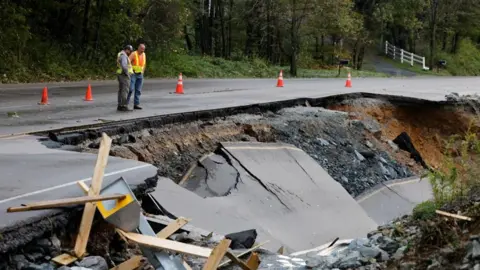 Workers survey a large section of Highway 105 that washed away because of flood waters during Tropical Storm Helene