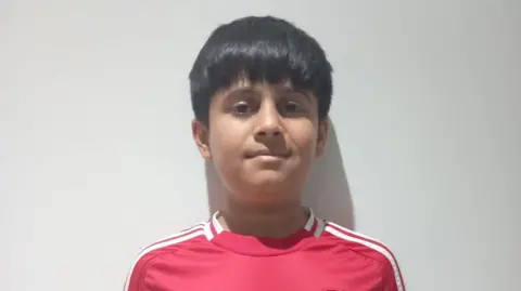 Family A boy with black hair in a Manchester United shirt standing against a white wall