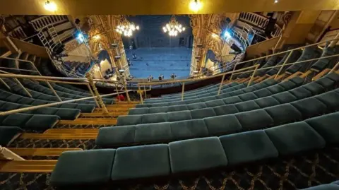 A view of the top gallery tier at Blackpool's Grand Theatre with rows of blue seats stretching off towards the stage below.