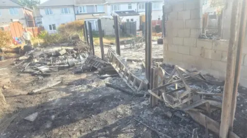 Tony Aldhouse A garden completely destroyed by fire with missing fence panels and debris everywhere. Everything is charred and blackened