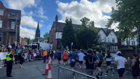 Crowds of people stood behind barriers watching as runners go past them.