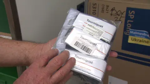 A person holds up a tourniquet, which is sealed in plastic packaging.